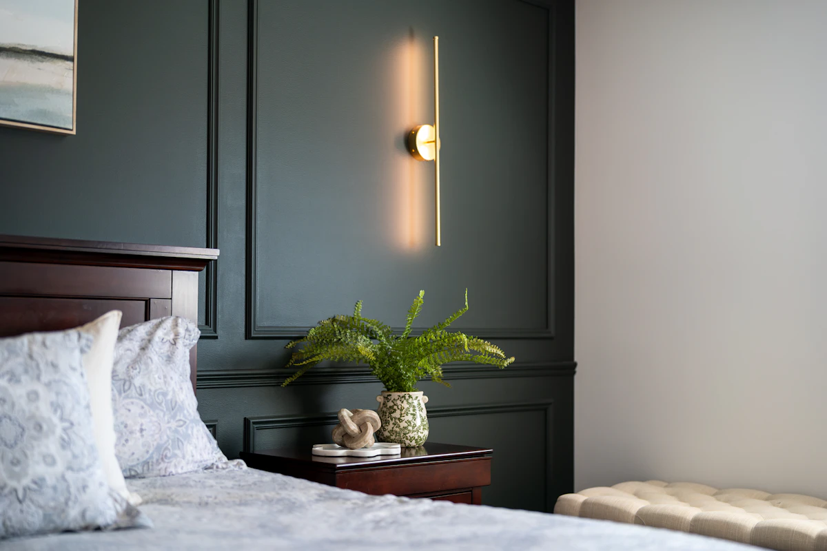 Modern bedroom with a dark green accent wall, bedside lighting, and a plant