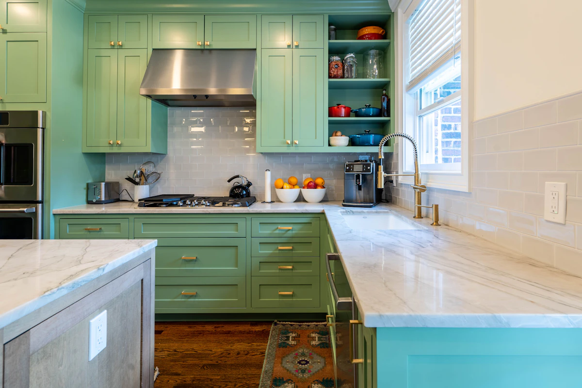 Green kitchen with a glossy tile backsplash, green cabinets, marble countertops and brass accents