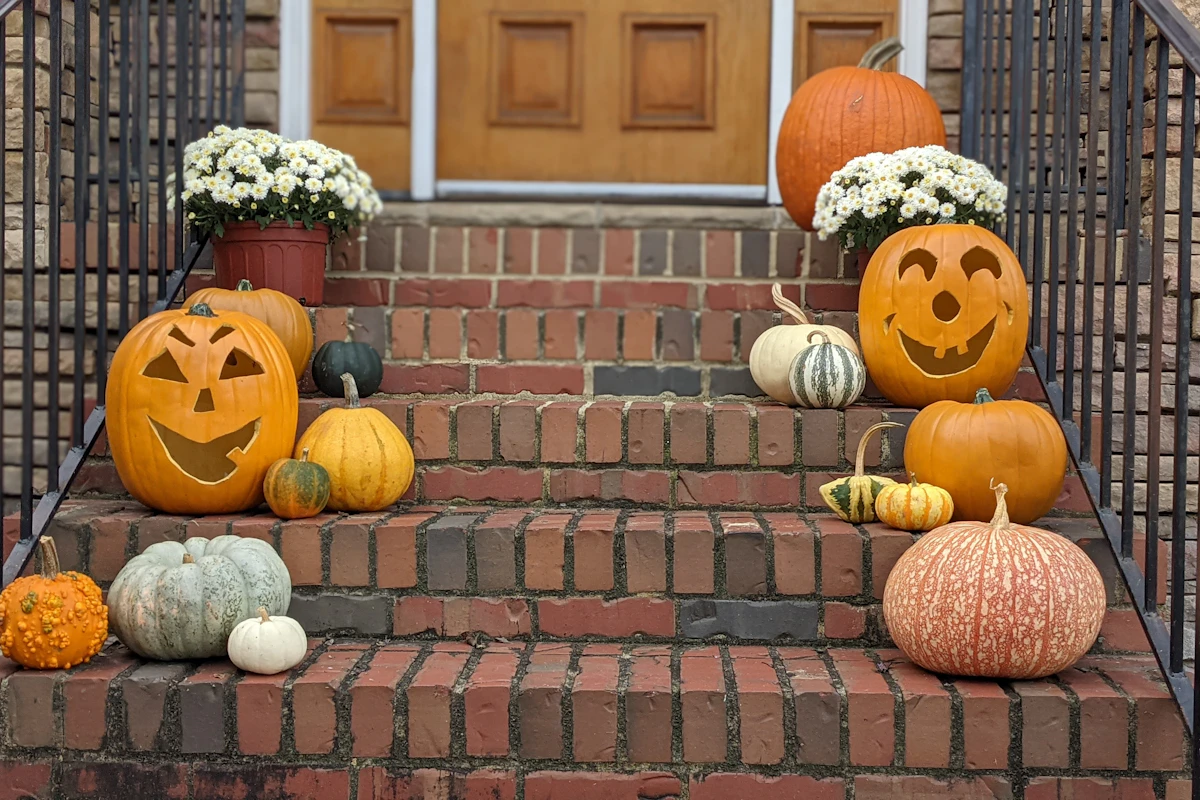 Front steps decorated with grouped pumpkins and flowers along the sides of the walkway