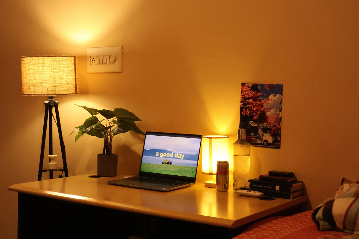 Small warm apartment workspace with laptop, lamp, and plant on a compact desk