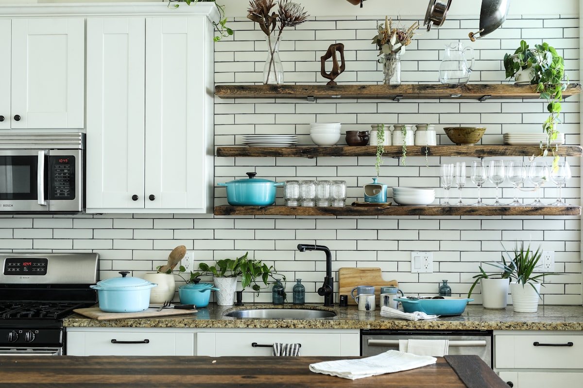 Small kitchen with white cabinets and open wooden shelves holding everyday cookware