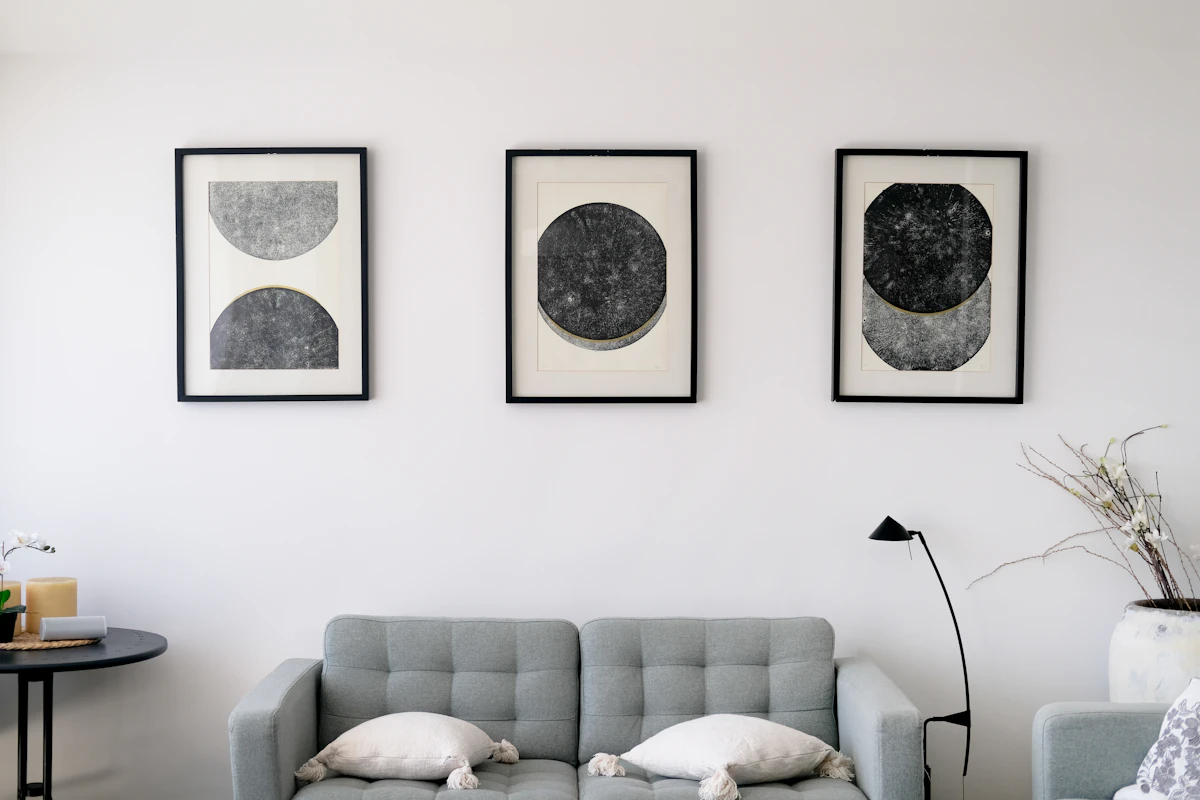 Three abstract framed art pieces arranged evenly above a gray sofa